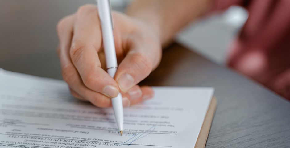 A hand signing an official document — the certification paperwork behind a government supplier registration