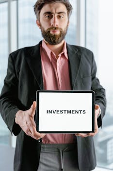 Businessman holding tablet displaying the word 'Investments' in an office setting.