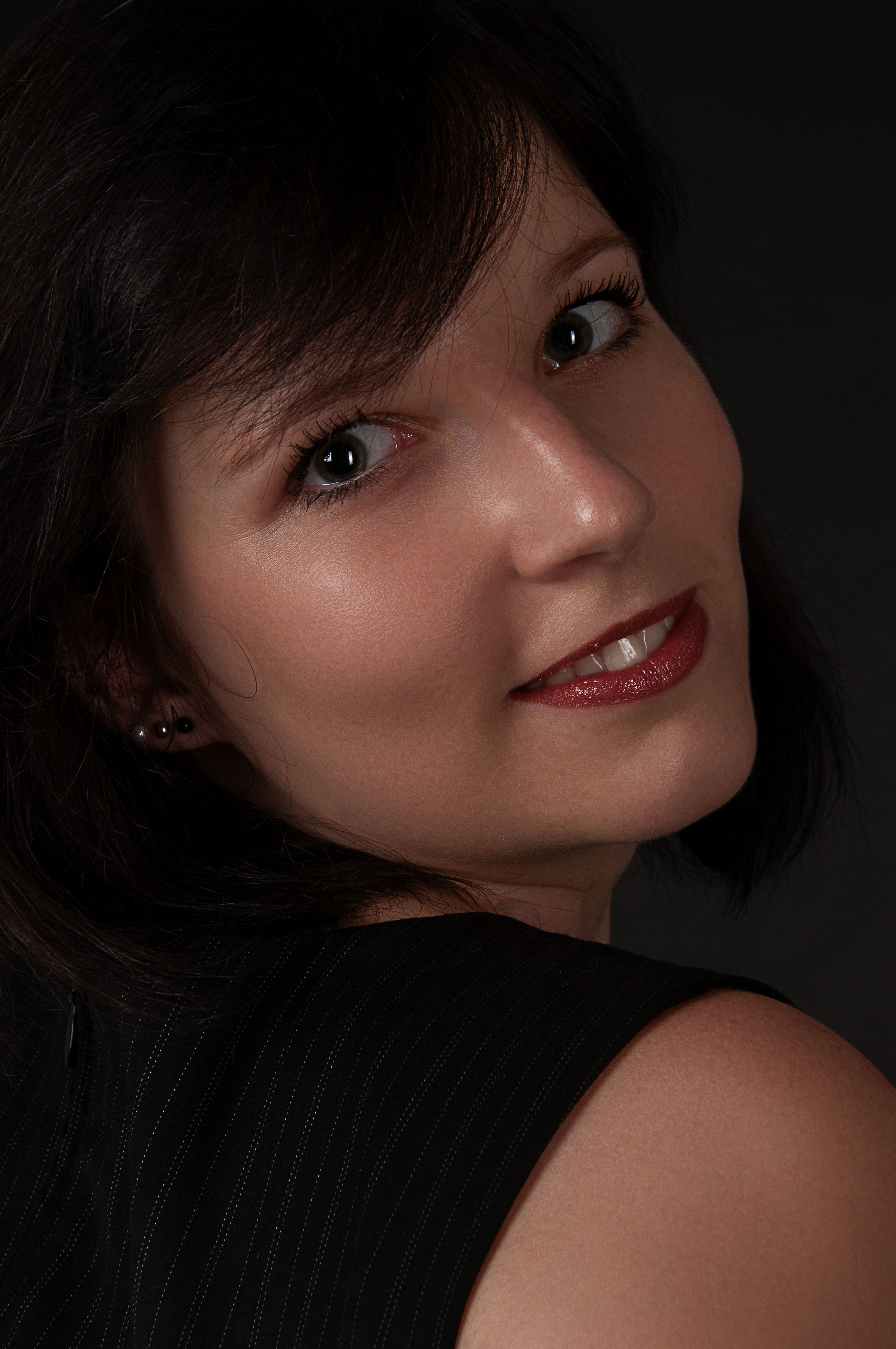 Close-up portrait of a smiling woman in Leipzig with dark background and elegant look.