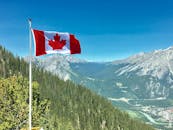 在风景优美的山景上，加拿大国旗随风飘扬，蓝天绿树成荫