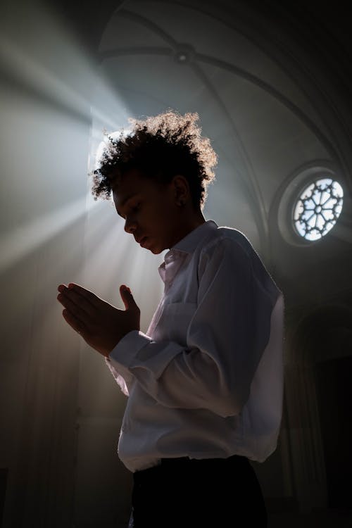 A Boy in White Polo Shirt Praying Inside a Church