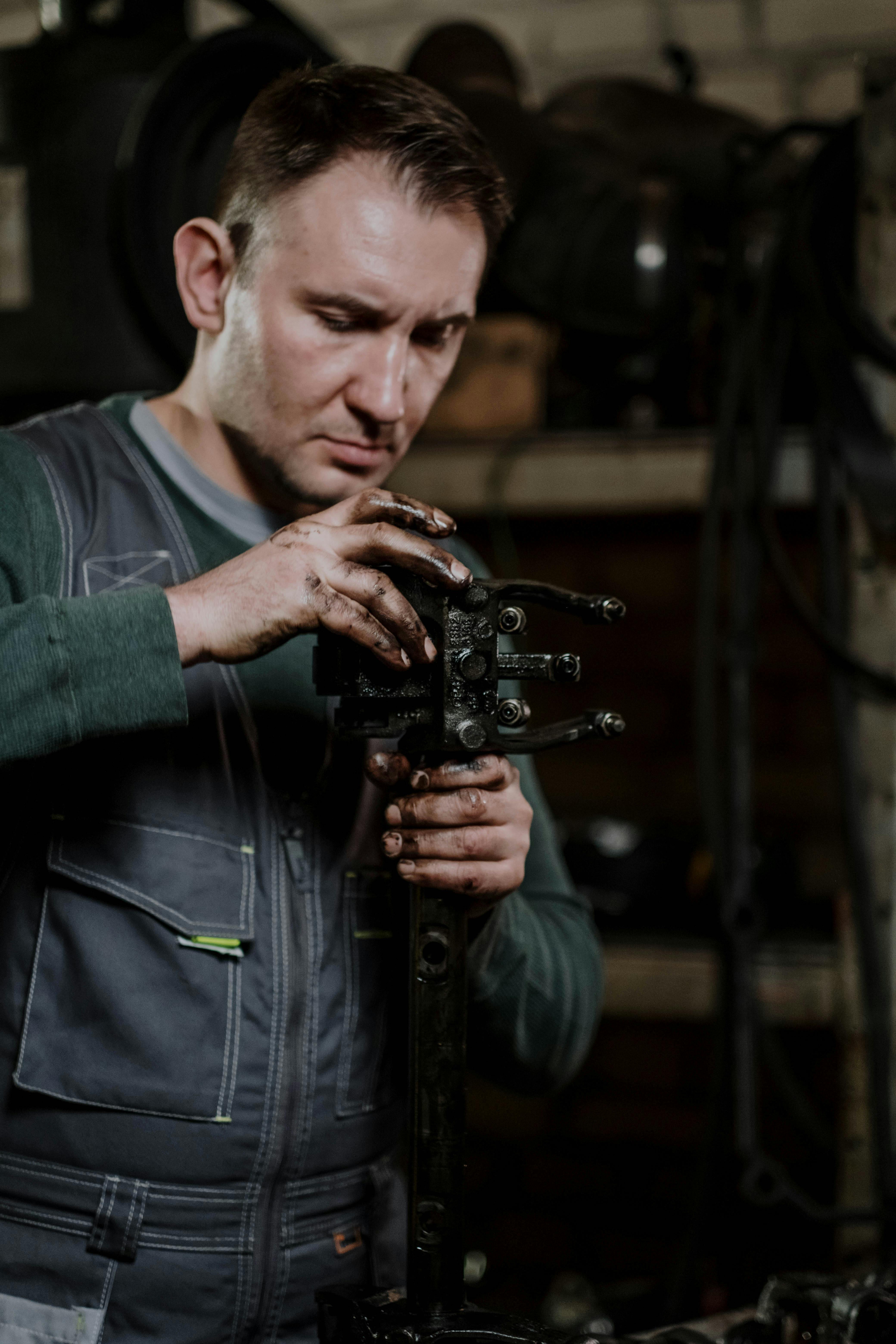 Mechanic concentrating on repairing a car component in a dimly lit workshop.