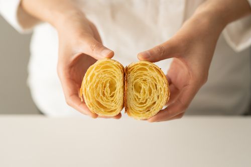 Free Detailed view of a croissant's layers, held by hands, showcasing its flaky texture. Stock Photo