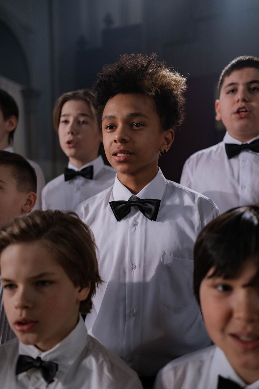 A diverse group of boys in uniform performing in a choir indoors.