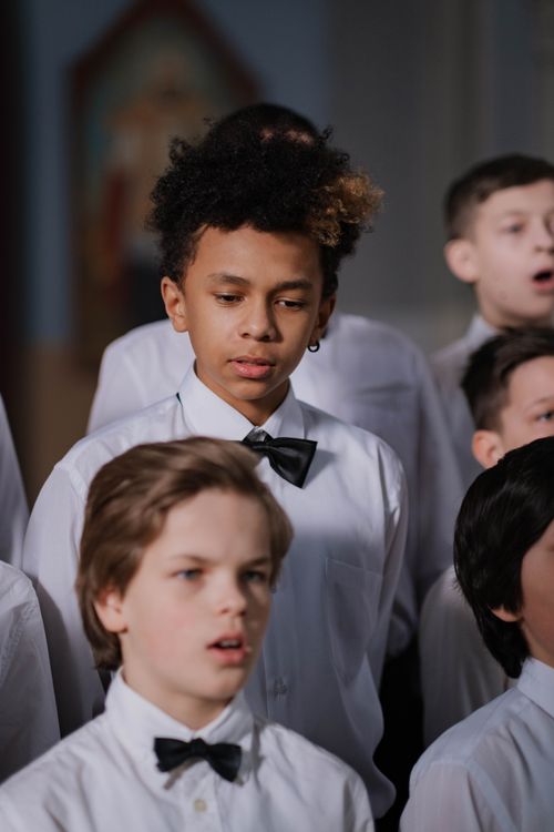 Free A diverse group of children in a choir wearing formal attire, singing together indoors. Stock Photo