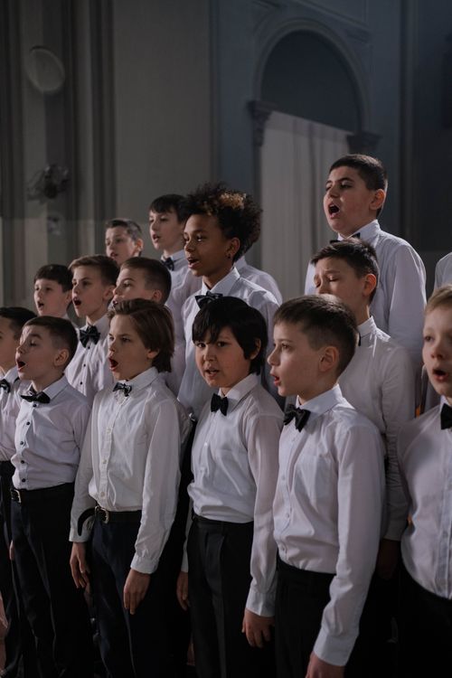 Free A group of diverse boys in uniform sing in harmony indoors, captured in a vertical shot. Stock Photo