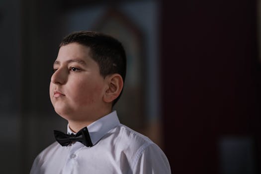 Close-up portrait of a young boy wearing a bow tie and white shirt indoors.
