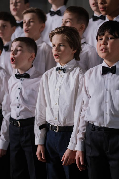 Free Group of boys in uniform singing together during choir practice. Formal attire with white shirts and bowties. Stock Photo