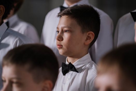 Close-up portrait of a boy wearing a bowtie, part of a children's choir.