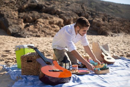 Free Young man setting up a picnic by the seaside with guitars in Portugal. Perfect for getaway inspiration. Stock Photo