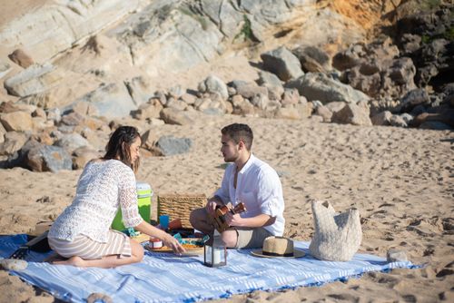 Free A couple enjoys a romantic picnic on a sandy beach in Portugal, with a ukulele. Stock Photo