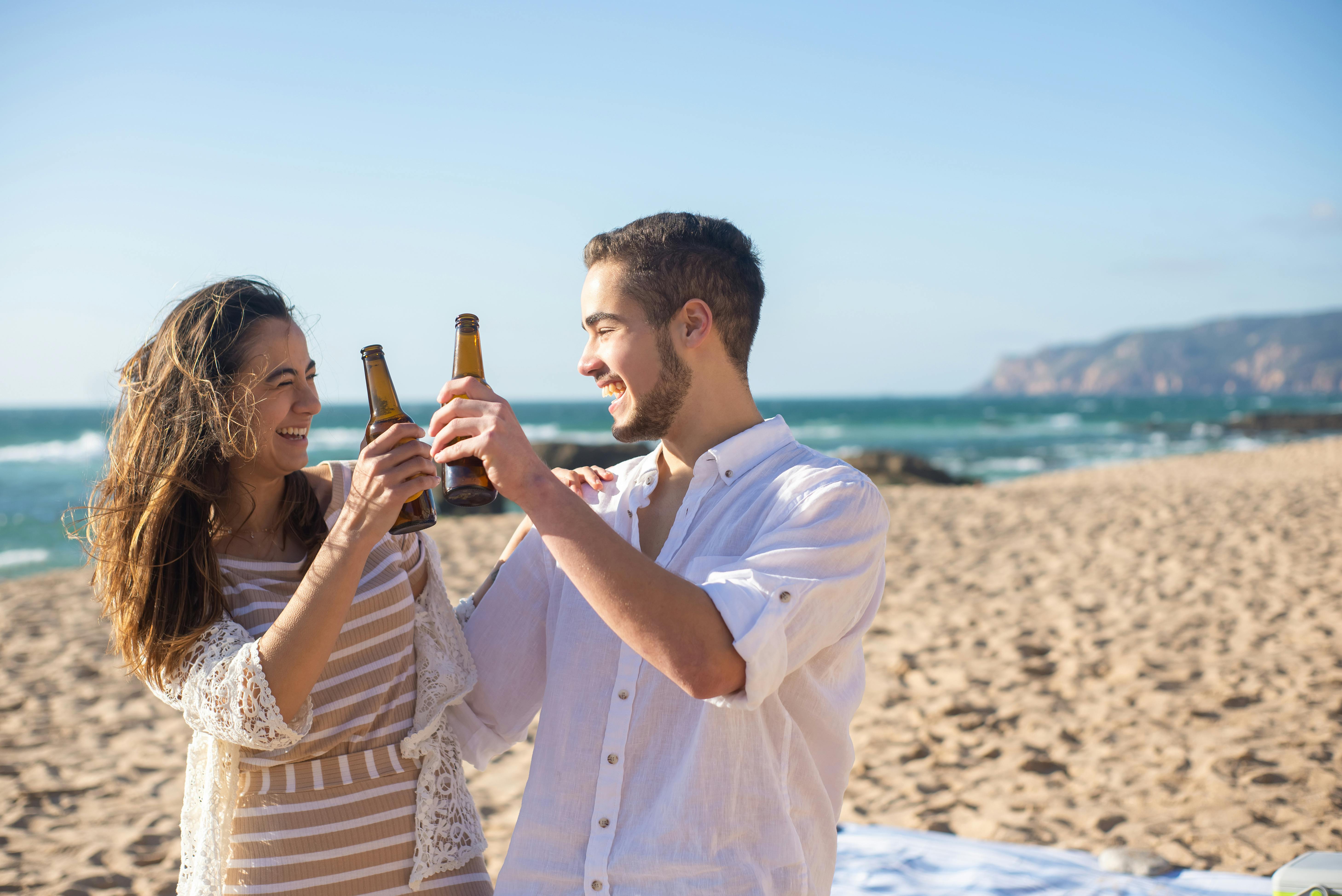 a man and woman holding beer bottles while looking at each other