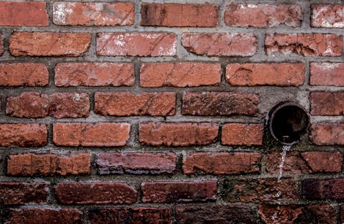 Drenaje De Tubería Marrón Redonda Con Líquido En Muro De Hormigón De Ladrillo Marrón