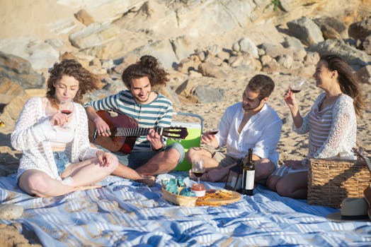 Group of friends having a beach picnic in Portugal, enjoying wine and music.