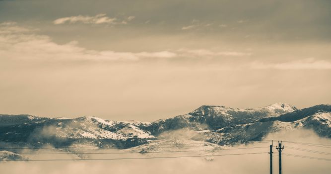 Scenic winter landscape with snow-covered mountains and power lines under a cloudy sky.