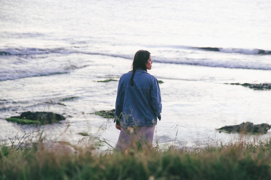 A woman in a denim jacket gazes out at the serene ocean, embodying a peaceful moment by the coast.