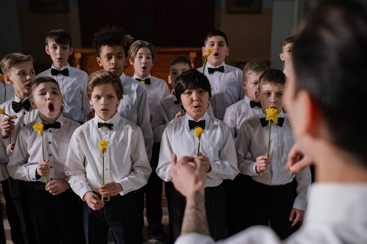 A Boys Choir Singing While Holding Yellow Flowers 