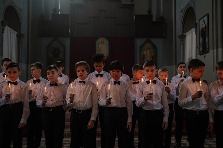 Boys In White Long Sleeves And Bowtie Holding A Lighted Candle