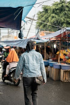 A bustling wet market with people walking, motorcycles, and denim-clad shopper.