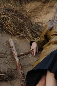 A woman in a brown coat lying on sand amid dry branches, evoking a moody and dramatic atmosphere.