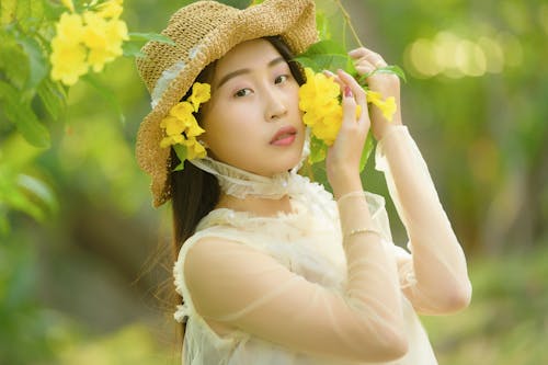 A Woman in White Long Sleeve Wearing a Brown Hat while Holding Yellow Flowers