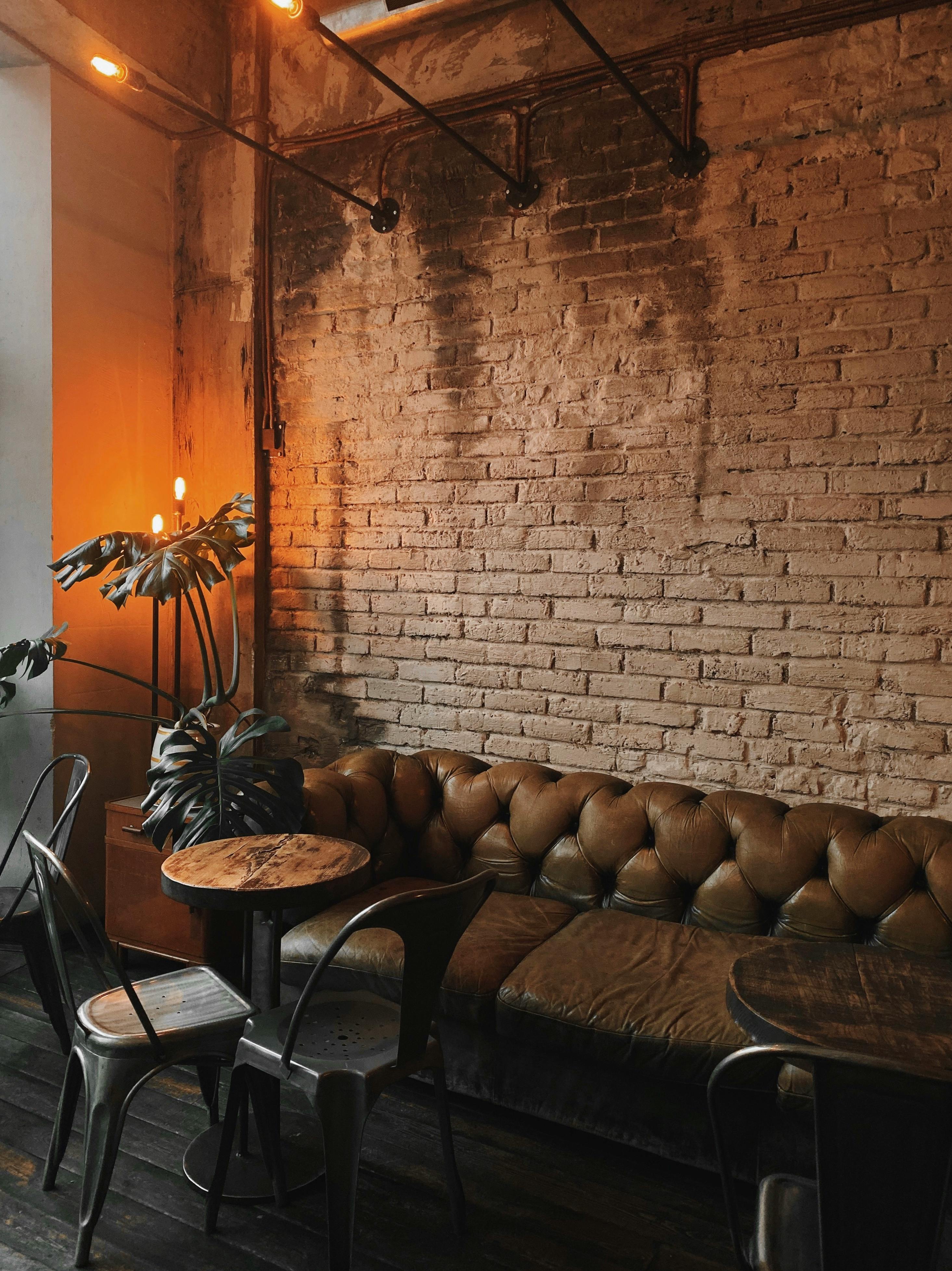 Free Warmly lit industrial cafe interior with leather seats, brick walls, and greenery for a cozy ambiance. Stock Photo