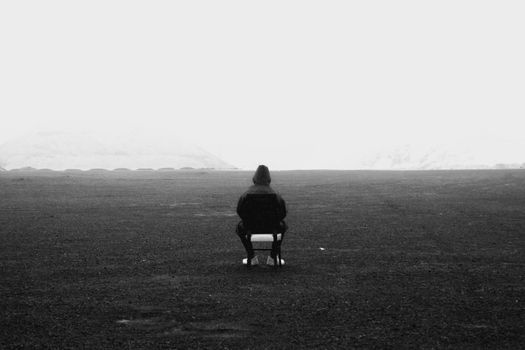 A lone person sitting on a chair in a vast grayscale landscape, evoking solitude.
