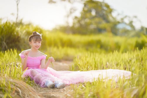 A Girl in Pink Dress Sitting on Green Grass Field