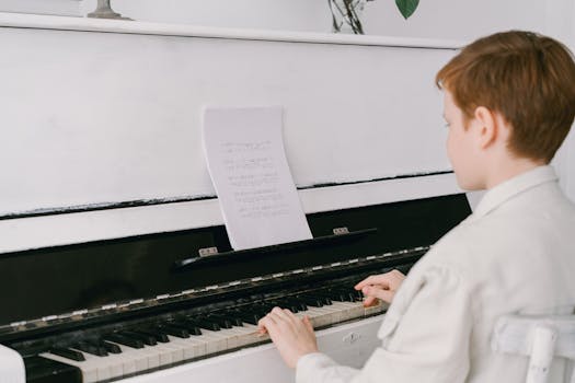 A young boy sits at an upright piano playing music indoors, focused on sheet music.