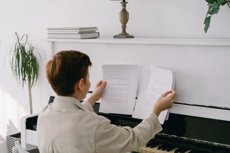 Boy Reading Music Sheets While Sitting At The Piano