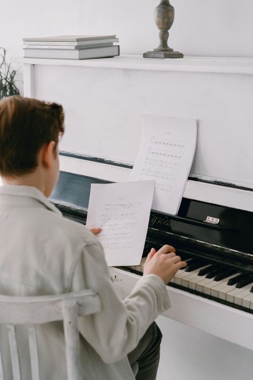 Free Man in gray coat practicing piano, focusing on sheet music in a cozy indoor setting. Stock Photo