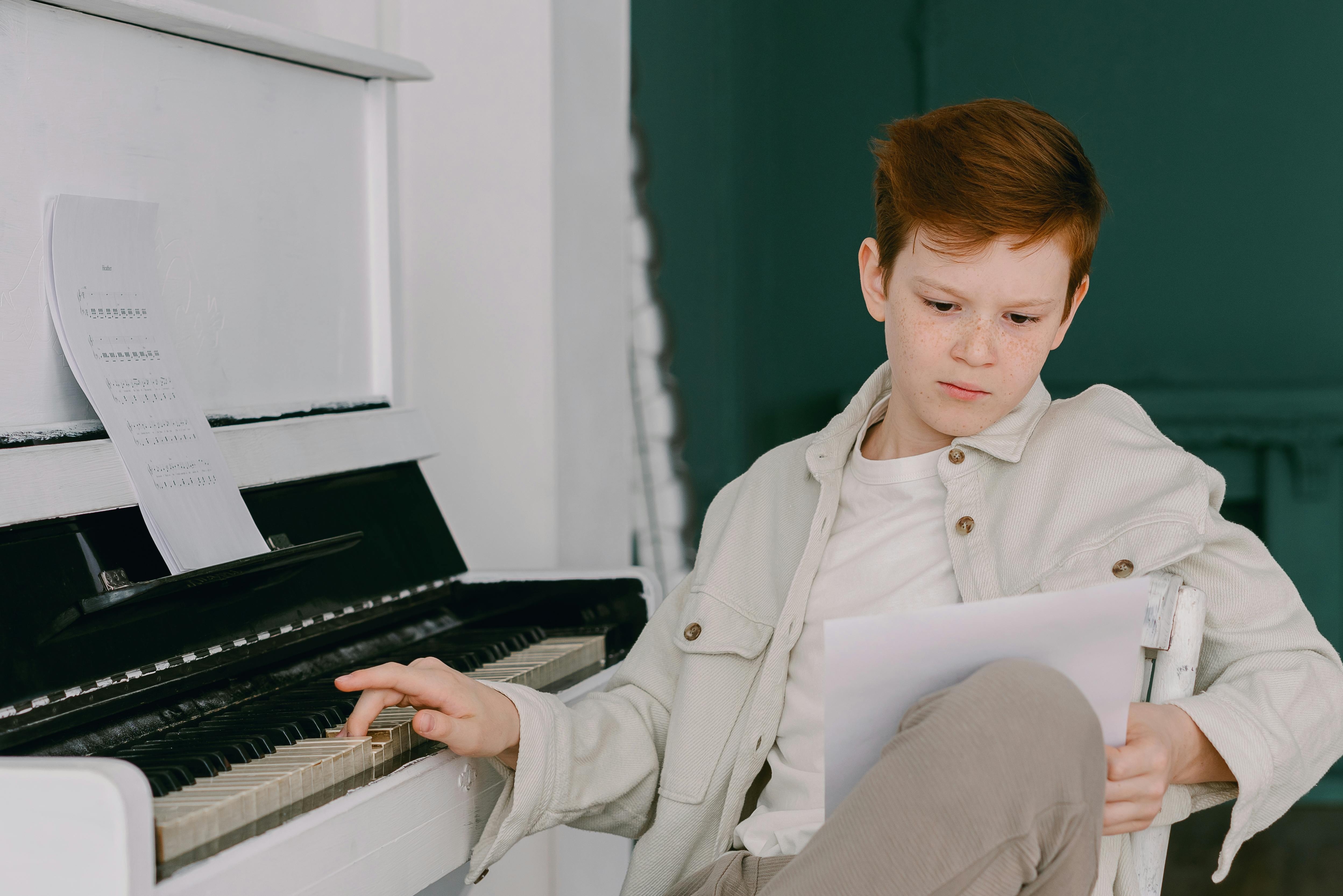 Foto de Young pianist boy looking at the digital tablet screen for learning piano  online at home. Music distance learning concept. do Stock