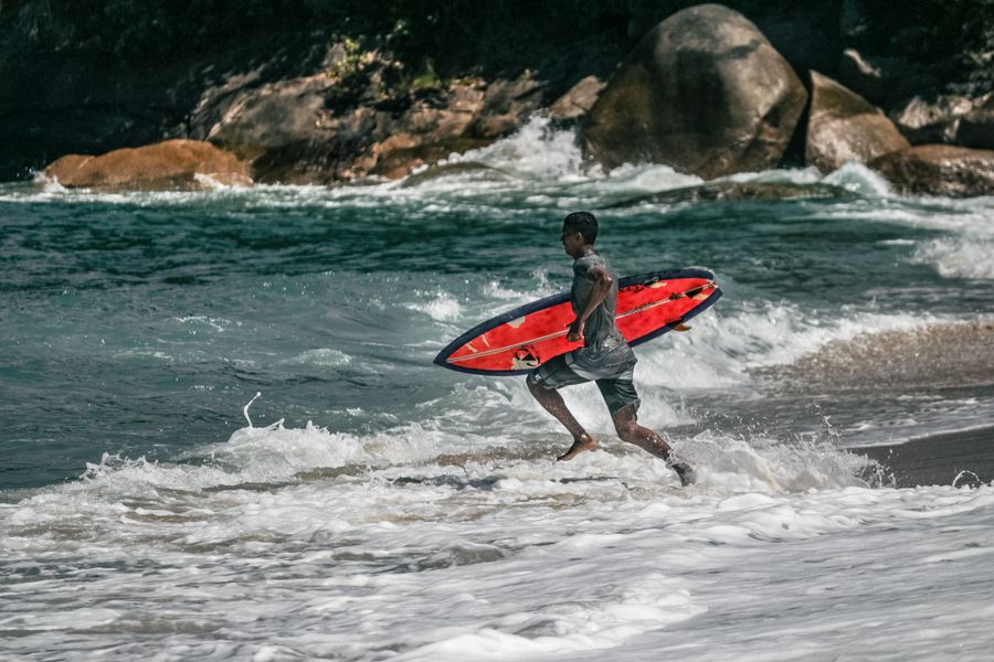 Surfer running through the waves with a red board