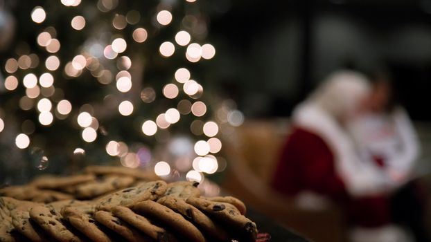 Close-up of chocolate chip cookies with holiday bokeh lights and Santa in the blurred background.