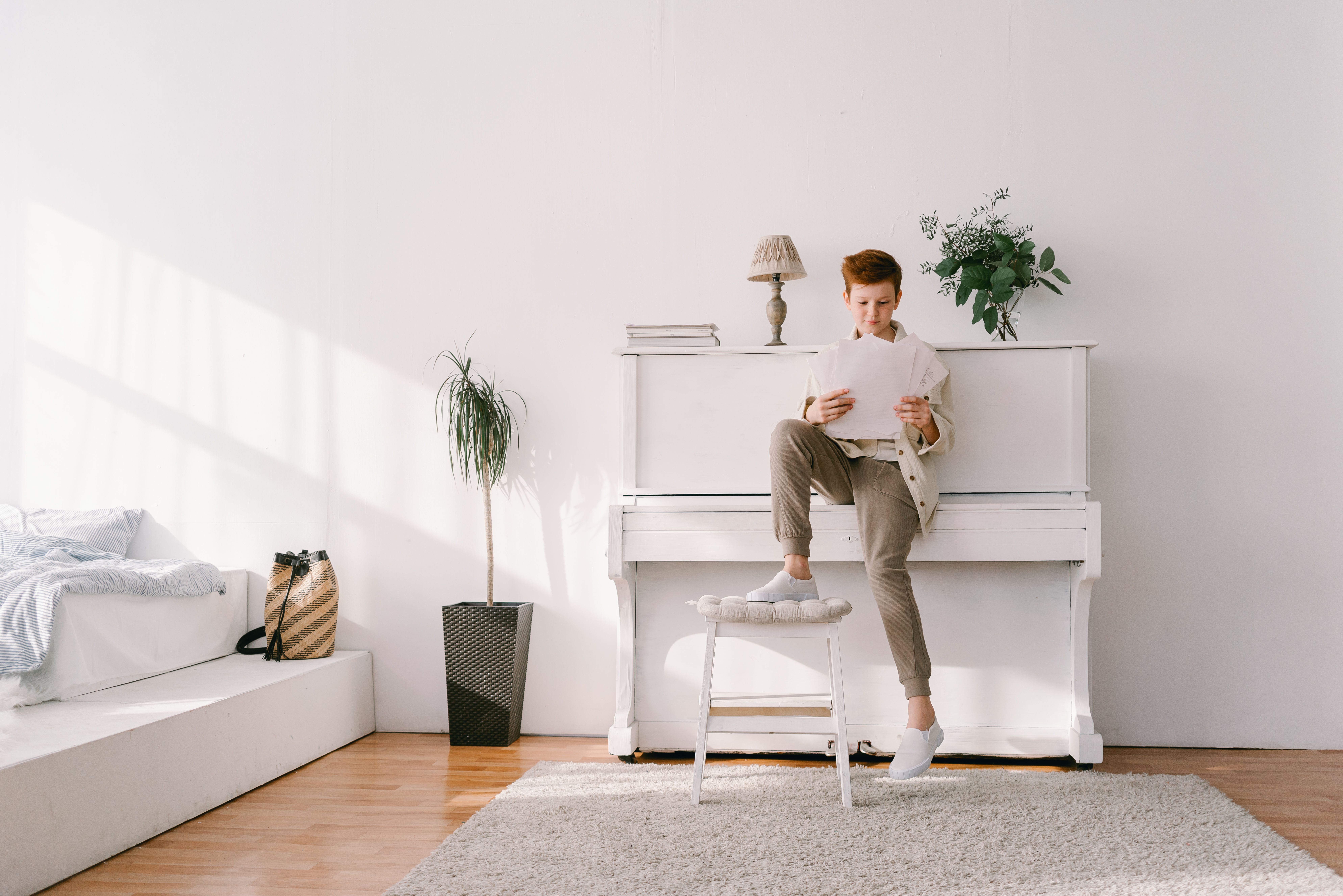 A young boy reading sheet music in a bright, minimalist room with a piano.