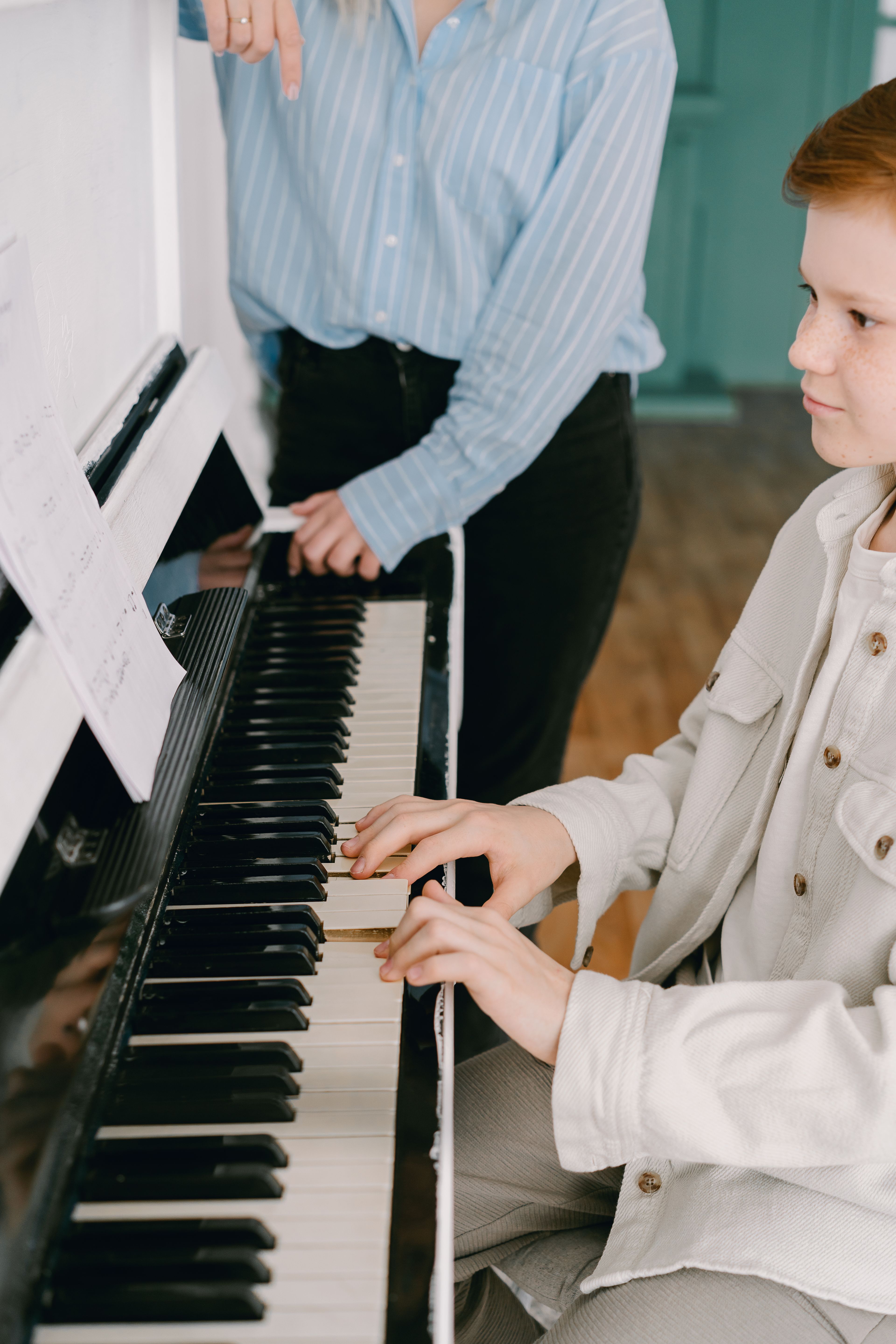 A young student at the piano with a teacher alongside