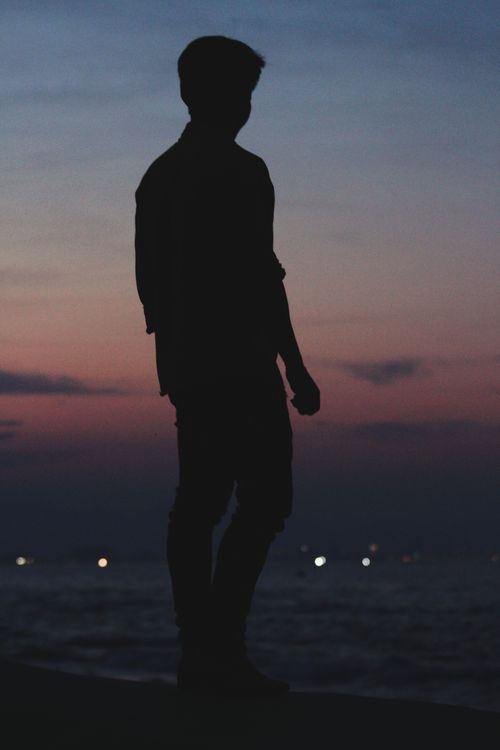Free A silhouette of a man standing against a vibrant sunset by the sea, capturing tranquility. Stock Photo