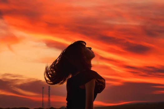 Capture of a woman's silhouette against a vividly colorful sunset sky featuring dramatic clouds.