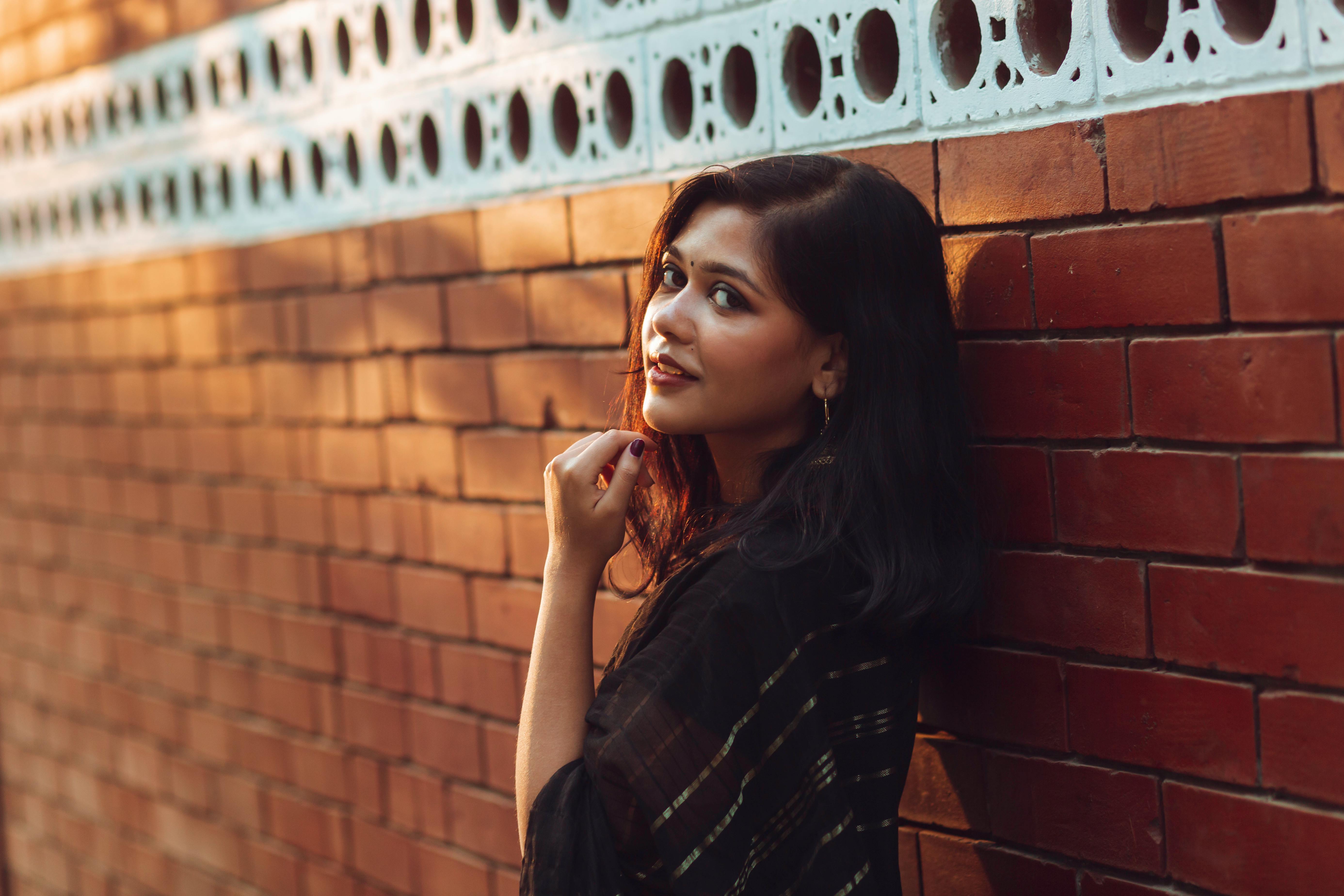 Charming portrait of a young woman leaning against a brick wall in Dhaka, Bangladesh.