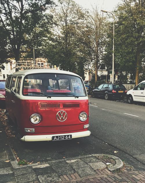 Free A vintage red Volkswagen combi van parked on a tree-lined street in a city environment. Stock Photo