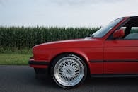 一辆经典红色合金车轮汽车的侧面图，停在乡村路旁的玉米地边