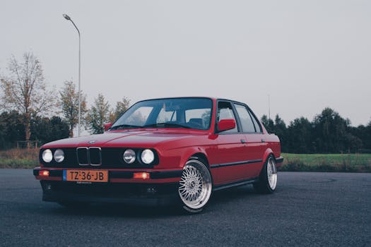 Classic red BMW E30 parked outdoors, showcasing its vintage style and chrome features.