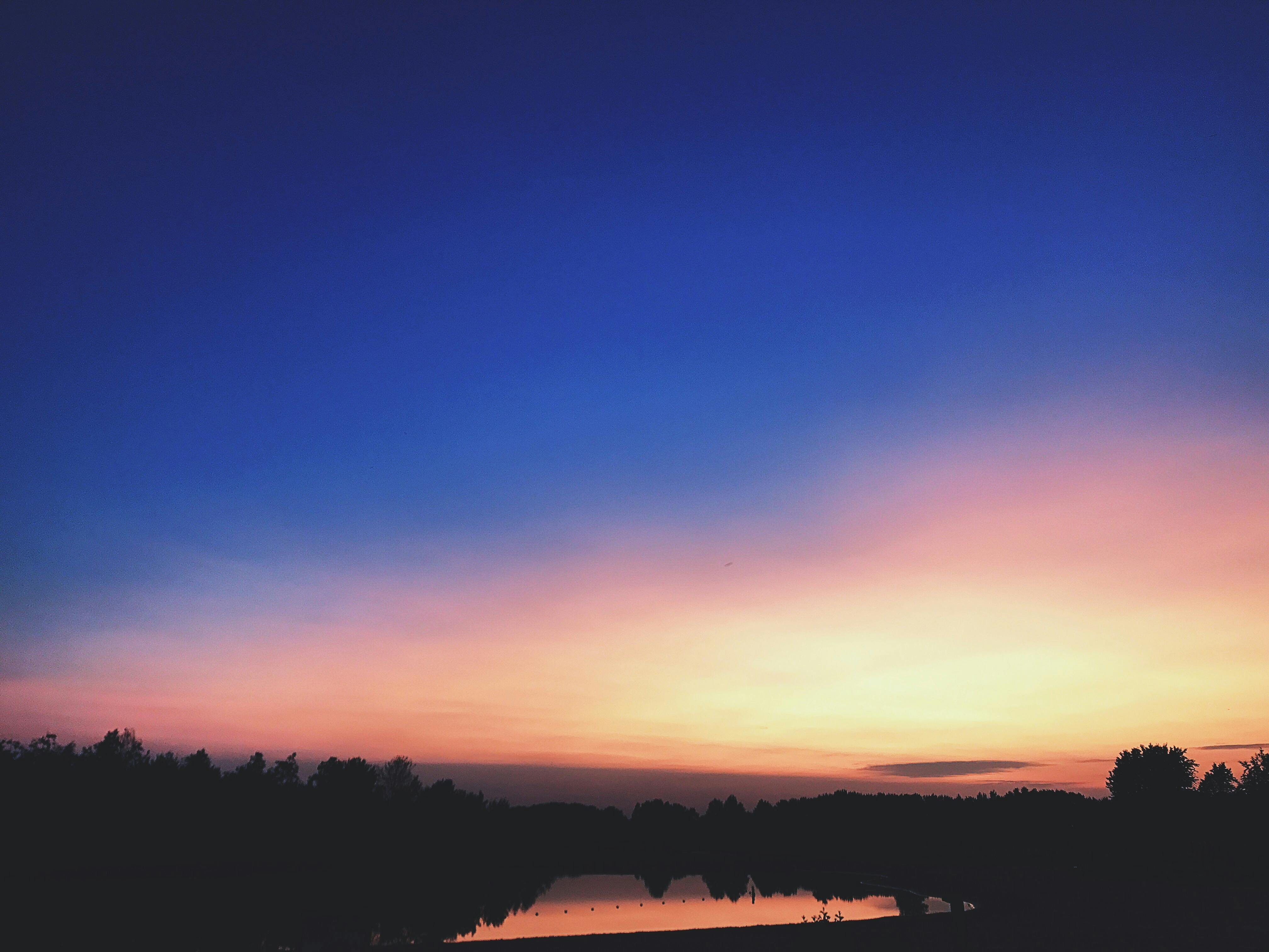 宁静的湖泊绿树环绕，倒映着色彩鲜艳、令人惊叹的日落