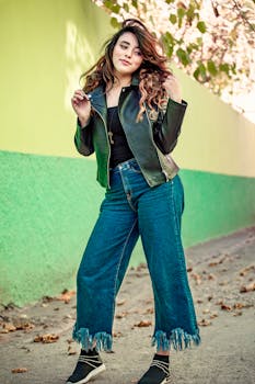 Stylish woman in denim and leather jacket posing against a colorful wall.
