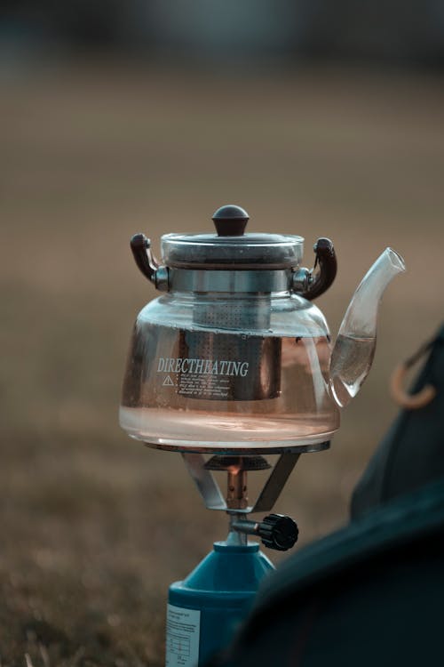 Glass teapot with water heating on gas burner at campsite during hike in nature