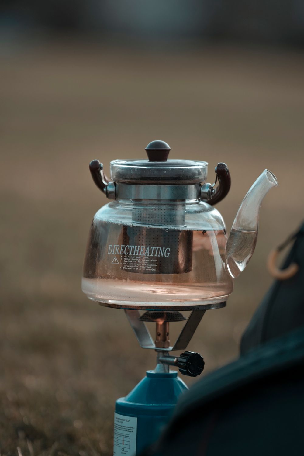 Glass kettle boiling water on a portable gas camping stove outdoors