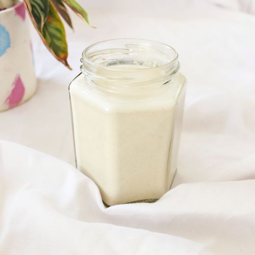 Free Close-up of creamy milk in a hexagonal glass jar with decorative plant, placed on white fabric indoors. Stock Photo