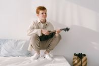 Boy Sitting on White Surface Holding Ukulele