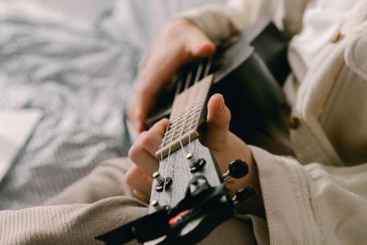 A detailed shot of a person playing a ukulele, captured with a shallow focus indoors.