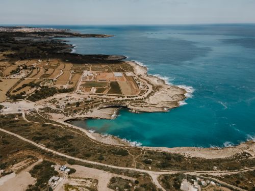 Free Stunning aerial view of Marsaxlokk coast with clear blue waters and rocky shores in Malta. Stock Photo